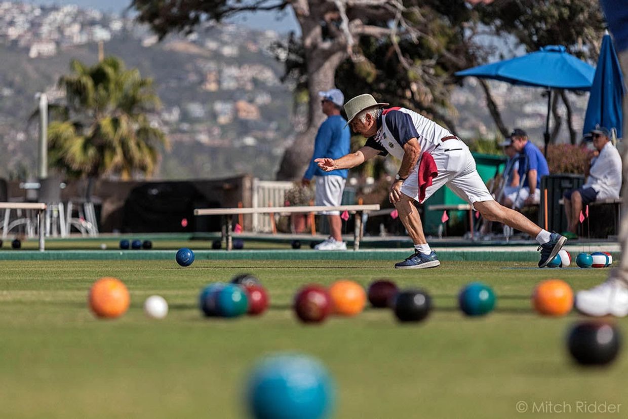 Bowler releasing bowl at ground level. Colorful bowls in foreground out of focus.