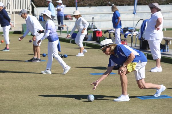 People playing lawn bowls on a sunny day, focusing on a woman about to roll a ball.