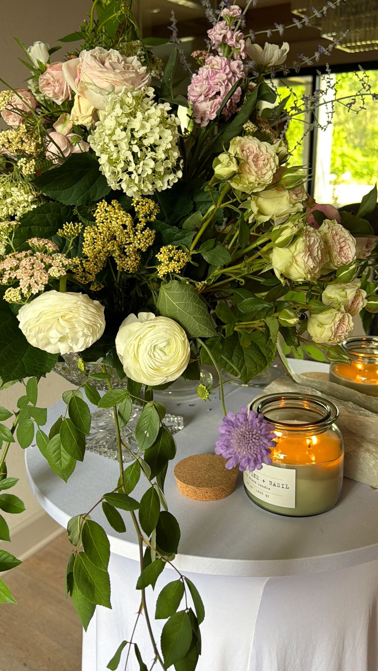 Elegant floral arrangement with soft pastel flowers and lit candles.