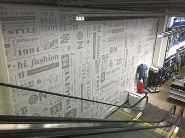 Inside a clothing store with escalators and fashion-themed wall decor.