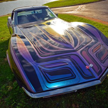 Classic Corvette with custom flame paint job parked on grass.