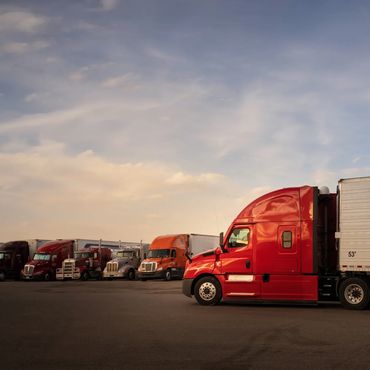 A red semi-truck trailer parked with other trucks at sunset.