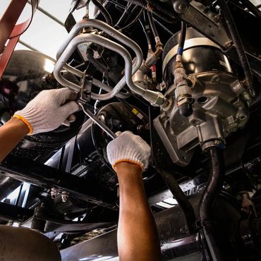A mechanic wearing gloves repairs vehicle parts underneath a car.