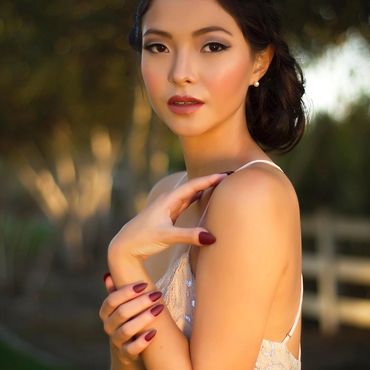 Elegant woman posing outdoors with soft lighting and makeup.
