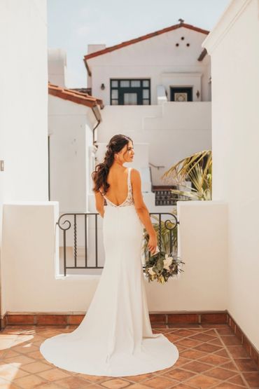 Bride in a white dress holding a bouquet on a sunlit terrace.