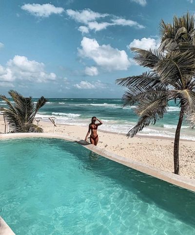 Woman standing by pool in front of sandy beach and Caribbean sea