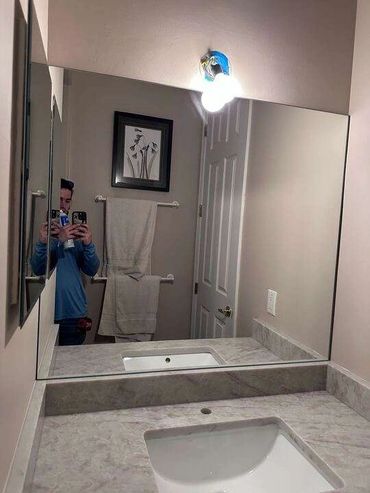 Man taking a selfie in a bathroom mirror holding two phones.