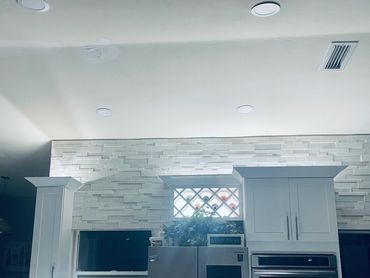 Modern kitchen with stainless steel appliances and white cabinetry under bright ceiling lights.