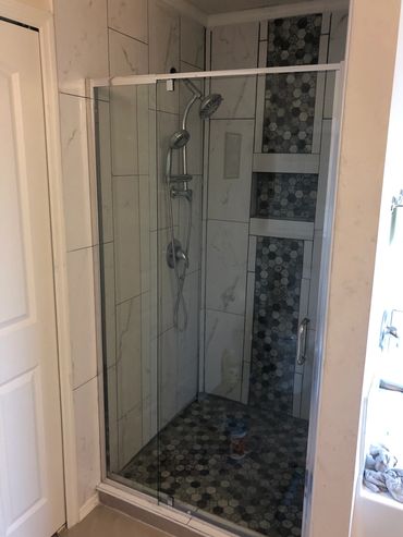 Modern walk-in shower with glass door and hexagonal tile accents.