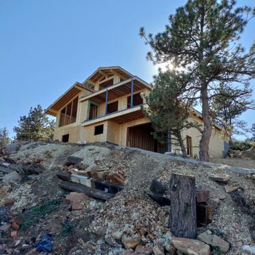 Wood-framed house under construction on a rocky hillside with trees.