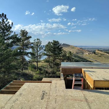 Construction site overlooking a scenic mountain and forest landscape under a blue sky.