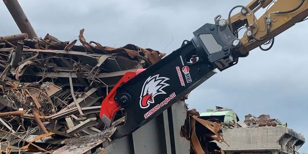 Excavator attachment tearing through metal debris at demolition site.