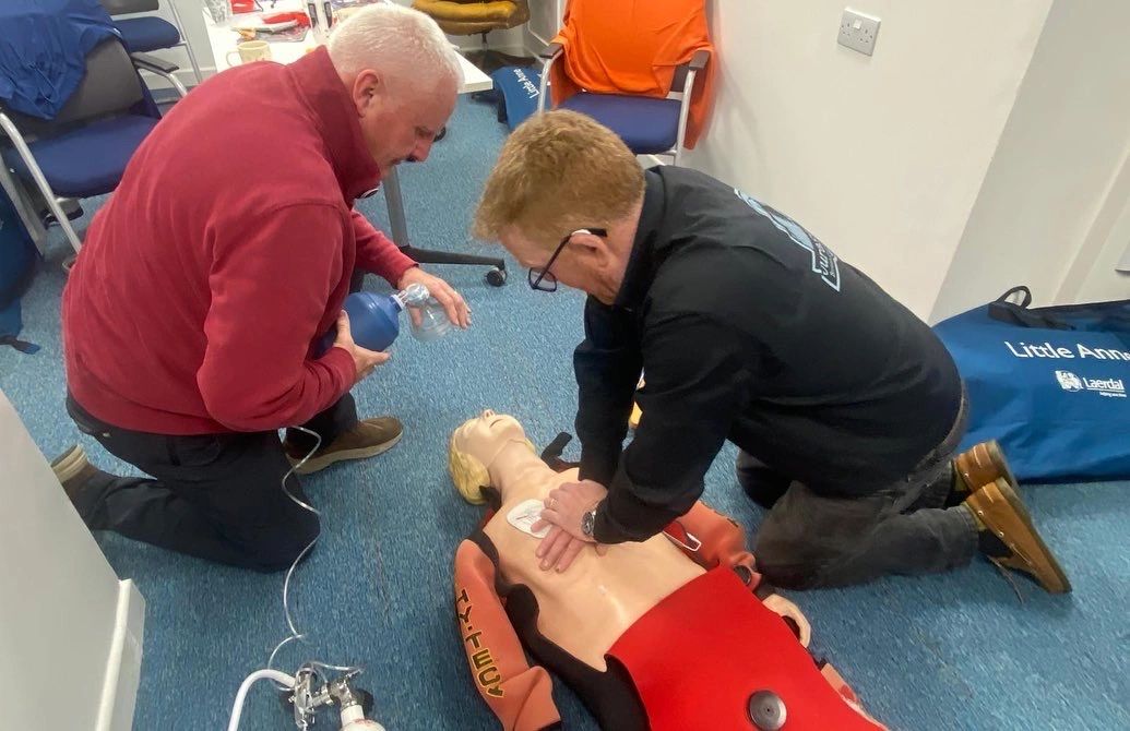 Two students practising chest compressions and bag valve mask ventilation on a manikin in a drysuit