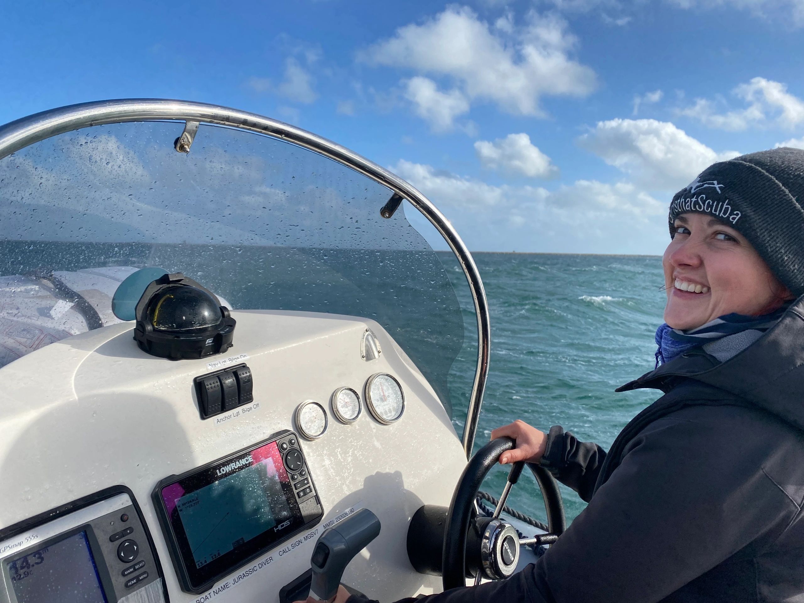 Smiling person steering a boat on a sunny day.