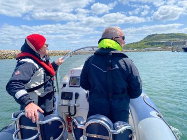 Two people standing at the helm of a RIB in Portland Harbour during training