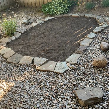 A garden bed bordered by flat stones with soil inside and surrounded by gravel.