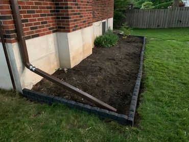 Freshly prepared garden bed beside a brick house with a downspout.