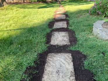 A stone pathway with freshly laid soil edges in a grassy yard.