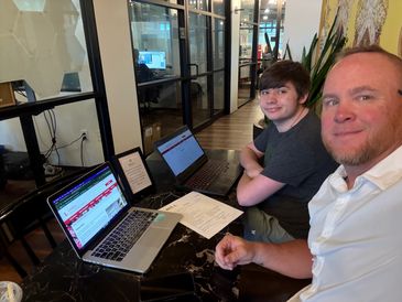 Two men working on laptops at a table in an office setting.