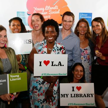 Trish at a L.A. Public Library event, standing with a group before the step and repeat, holding a si