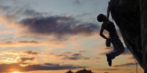 Silhouette of a rock climber against sunset sky.