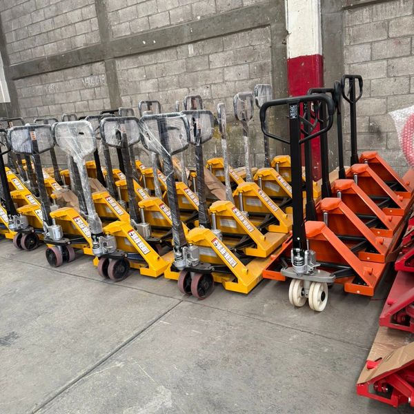 A row of yellow and orange pallet jacks lined up indoors.