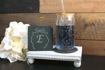 Decorative setup with a floral glass and monogrammed stone on a white stand.
