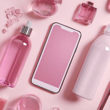 Flat lay of pink beauty products and a smartphone on a pastel pink background.