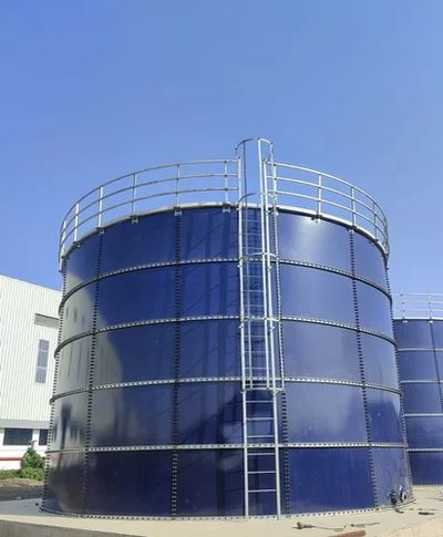 Large blue industrial storage tank with safety railing and ladder under clear sky.