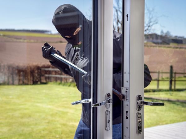 Burglar or thief breaking into a home through window with a crowbar