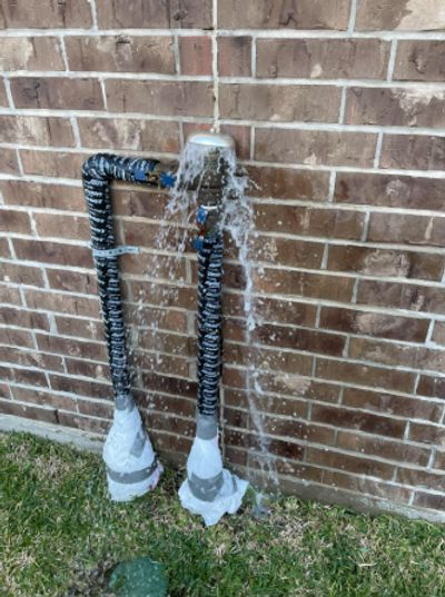 Leaking outdoor pipe spraying water against brick wall.