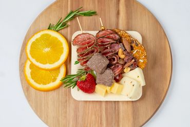 Charcuterie board with salami, cheese, nuts, chocolate, and fruit on a wooden platter.