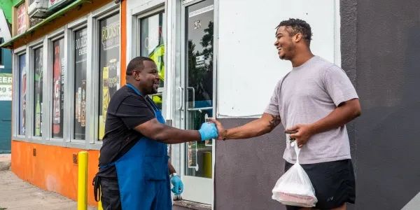 Two men smiling and shaking hands outside a store.