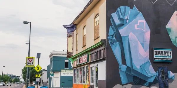 Colorful mural on building corner in urban street scene with shops and traffic signs.