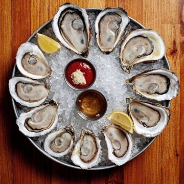 A dozen oysters on the half shell arranged in a circle on top of a bed of ice.