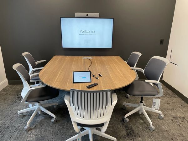 Modern conference room with six chairs, a wooden table, and a wall-mounted screen.