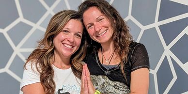 Two smiling women posing happily in front of a geometric wall.