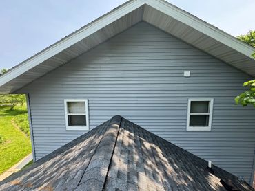 Gray house siding with shingles and two windows under a clear sky.