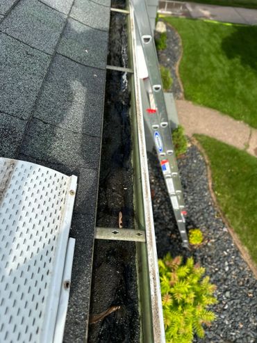 Dirty gutter filled with debris and a ladder beside the roof.