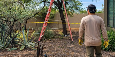 Man in gloves standing outside near a ladder and caution tape.