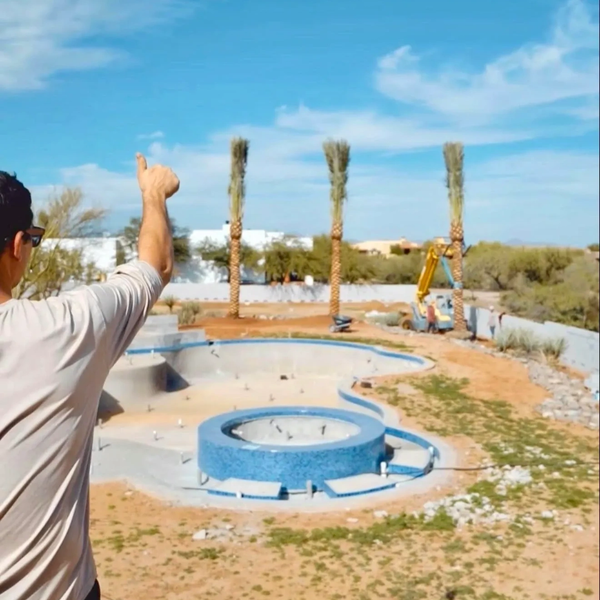 Man giving thumbs up near an unfinished pool under a clear sky.