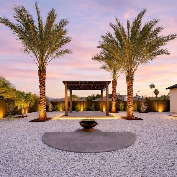 Backyard with palm trees and a fire pit at sunset.