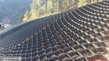 Black geocell grid installed on a slope with forest background.