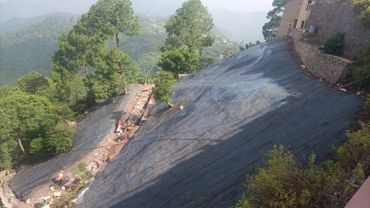A steep hillside covered with black tarp and a person working near trees.