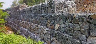 Layered gabion walls made of wire mesh filled with rocks on a hillside.