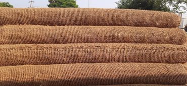 Stacked rolls of coarse jute fabric outdoors under sunlight.