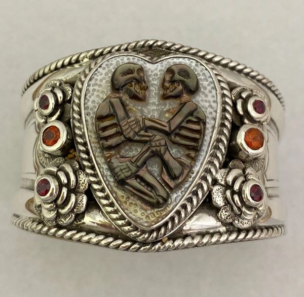 carved silver bracelet cuff with red and orange stones and two carved skeletons of pearl in center
