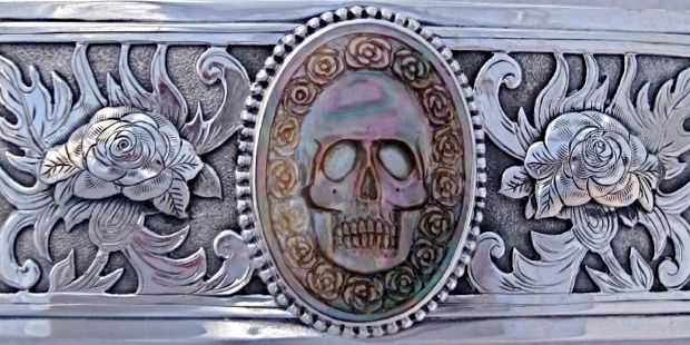 rectangular image of carved buckle with floral texture and mother of pearl carved skull in center