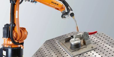 An orange KUKA robotic arm performing precision welding on a metal surface.