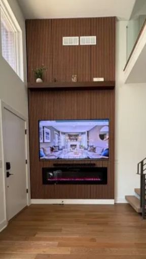 Floor to ceiling custom media wall with 85in TV, sound bar, electric fireplace and floating shelf.